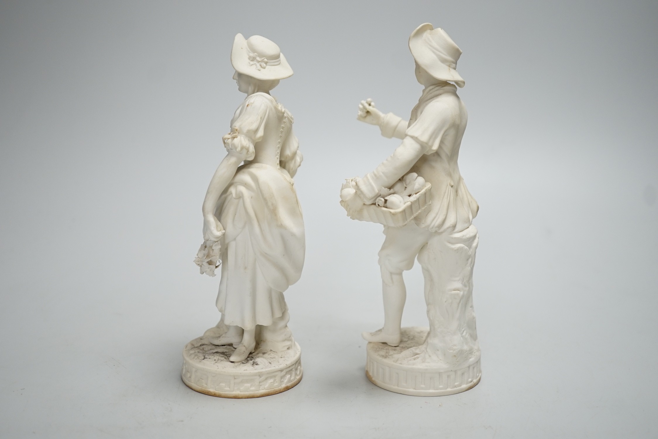 A pair of Minton biscuit figures of a boy and girl with flowers, on circular bases, 19cm